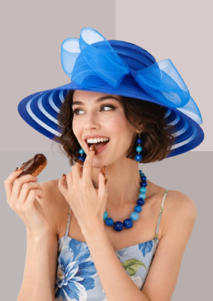 Femme brune, mangeant un éclair au chocolat et se léchant les doigts, en tenue de réception: robe bleue à fleurs et capeline bleu France | Cap-Chapeau